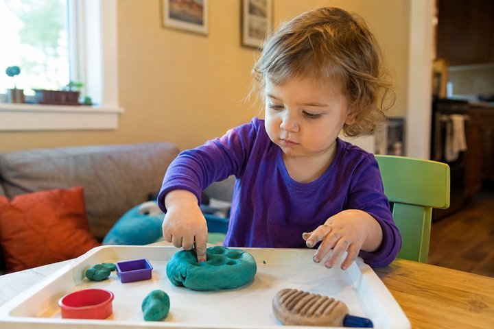A 2-year-old squashing and poking a lump of playdough on a tray